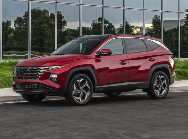 Side view of a red 2023 Hyundai Tucson parked in front of a modern building with reflective glass windows.